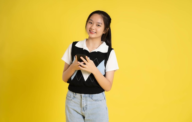 Portrait d'une belle fille asiatique utilisant un téléphone sur fond jaune