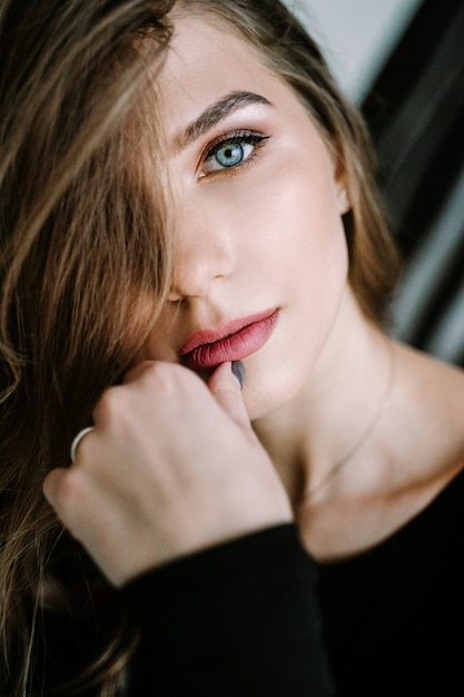 Portrait d'une belle fille aux cheveux longs brun clair dans un t-shirt noir et un jean dans les escaliers de la maison. Beaux yeux bleus