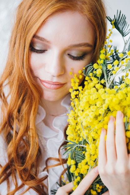 Portrait d'une belle fille aux cheveux roux avec un Mimosa dans une longue robe blanche