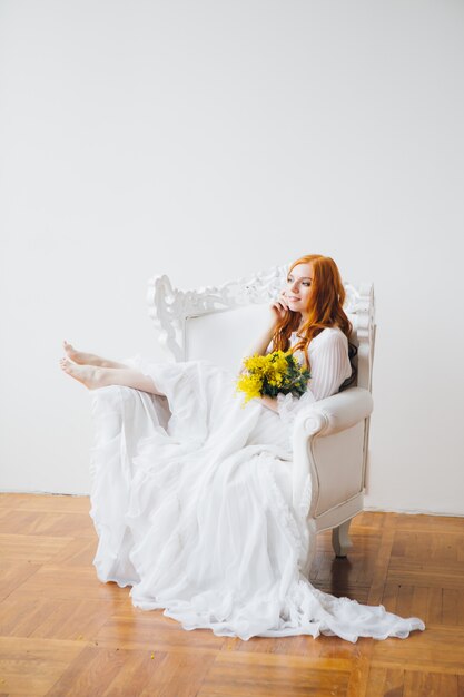 Portrait d'une belle fille aux cheveux roux avec un Mimosa dans une longue robe blanche