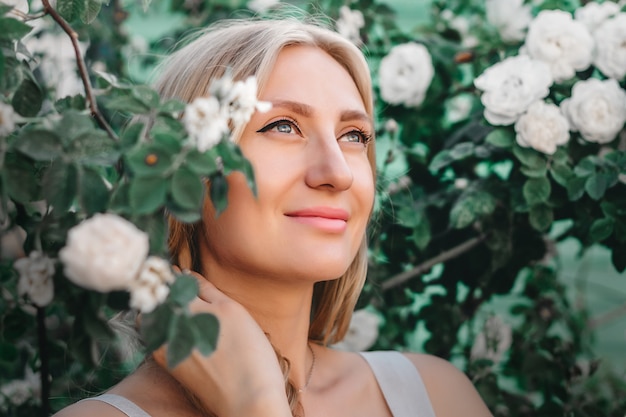 Portrait d&#39;une belle fille blonde avec une coiffure sur le fond d&#39;un buisson de roses blanches