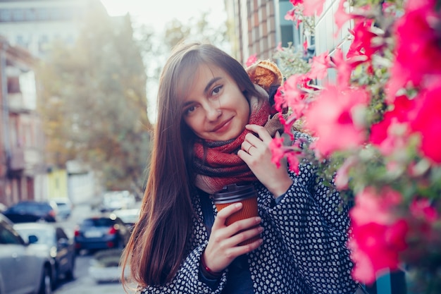 Portrait de belle fille brune avec boisson à emporter dans la rue. écharpe et manteau d'automne dans la ville. Vue imprenable sur une femme d'affaires avec une tasse de café marchant dans la rue de la ville.