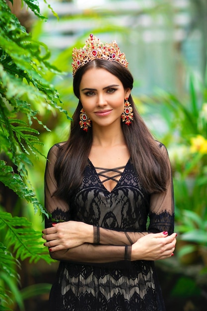 Portrait d'une belle fille brune en couronne rouge debout dans un jardin sur fond vert