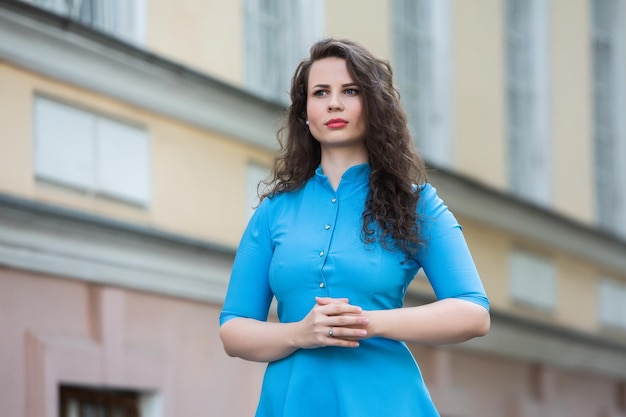 Portrait d'une belle fille brune européenne blanche vêtue d'une robe bleue dans la rue en été