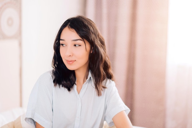 Portrait d'une belle fille caucasienne rêveuse avec un maquillage naturel, en pyjama assis dans son lit à l'hôtel, souriant en détournant les yeux, se souvenant de la date avec son petit ami. Temps du matin, détente. Copiez l'espace.