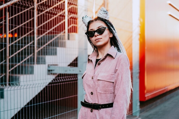 Portrait de belle fille cool sur mur urbain. Journée ensoleillée. Fille en lunettes de soleil et combinaison rose