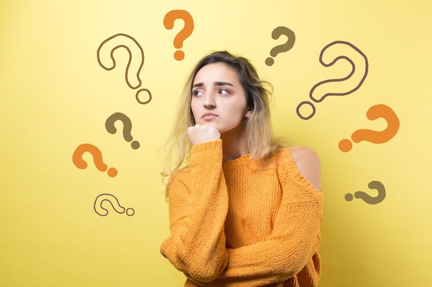 Le portrait d'une belle fille dans un chandail orange regarde de côté avec une expression pensive