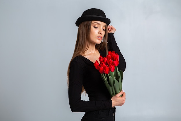 Portrait d'une belle fille dans un chapeau avec des tulipes dans les mains en studio