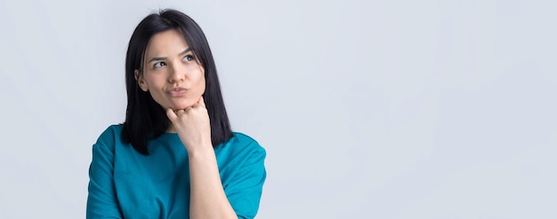 Le portrait d'une belle fille dans un t-shirt bleu regarde de côté avec une expression pensive envisage un plan d'action supplémentaire