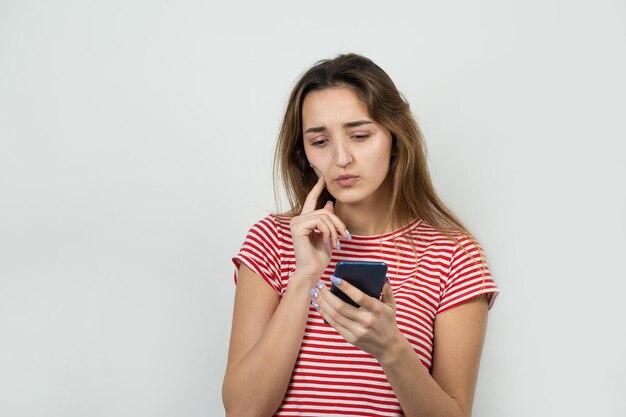 Le portrait d'une belle fille dans un t-shirt rayé regarde de côté avec une expression pensive envisage un plan d'action supplémentaire