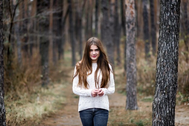 Portrait d&#39;une belle fille debout dans une forêt d&#39;automne et vêtue d&#39;un pull chaud blanc