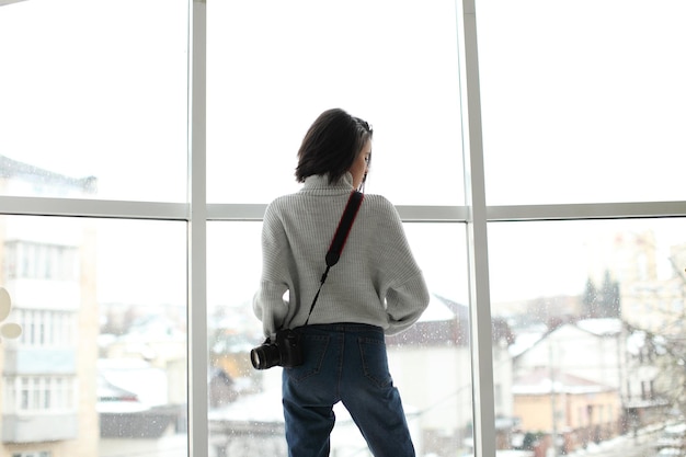 Portrait d'une belle fille hipster avec un appareil photo debout près de la fenêtre