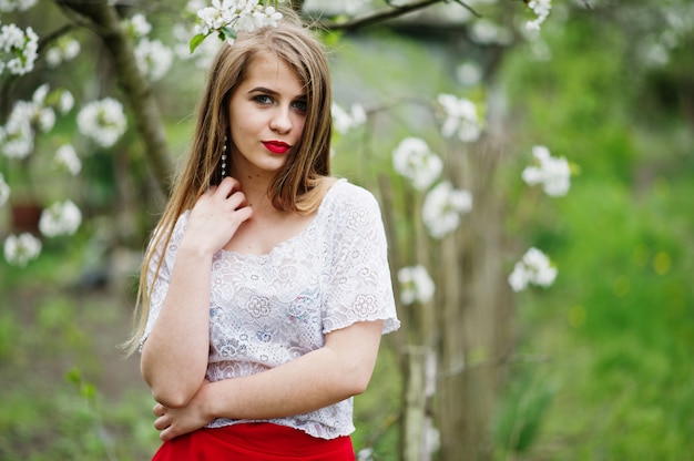 Portrait de belle fille avec des lèvres rouges au jardin de fleurs de printemps, porter sur une robe rouge et un chemisier blanc