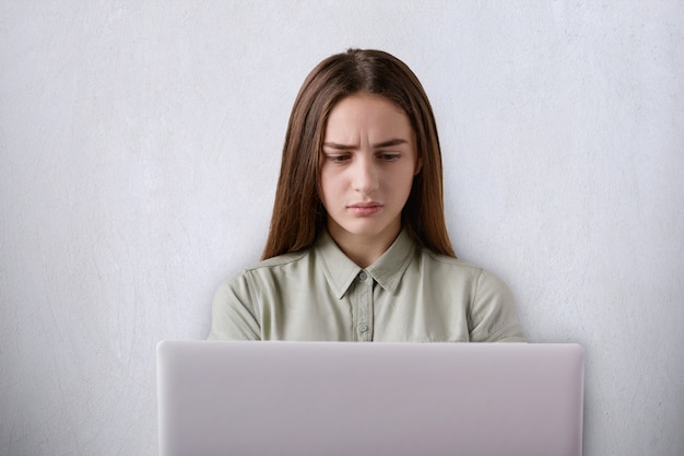 Un portrait de belle fille mécontente ayant une expression fatiguée travaillant avec son ordinateur portable