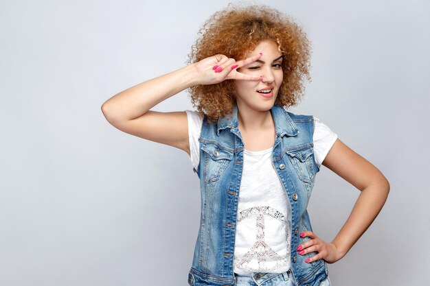 Portrait d'une belle fille métisse bouclée dans un style décontracté avec un signe v devant ses yeux