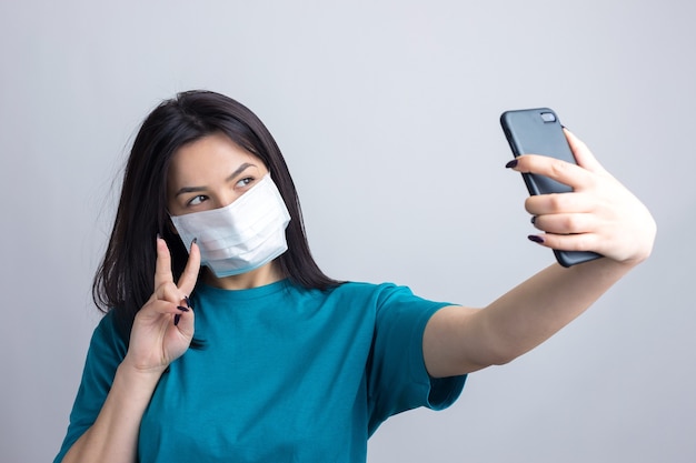 Portrait d'une belle fille prenant un selfie sur fond gris portant un masque médical.