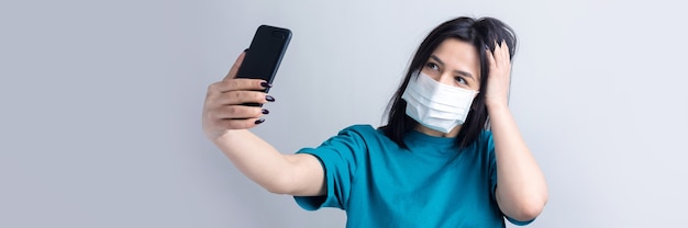 Portrait d'une belle fille prenant un selfie sur fond gris portant un masque médical.