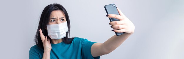 Portrait d'une belle fille prenant un selfie sur fond gris portant un masque médical.