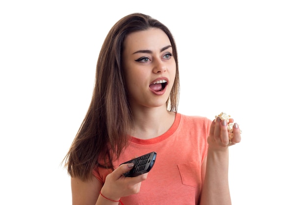 Portrait d'une belle fille qui mange du pop-corn et tenant une télécommande de télévision isolée sur un gros plan de fond blanc