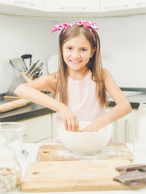 Portrait de belle fille souriante faisant de la pâte à tarte dans un bol blanc