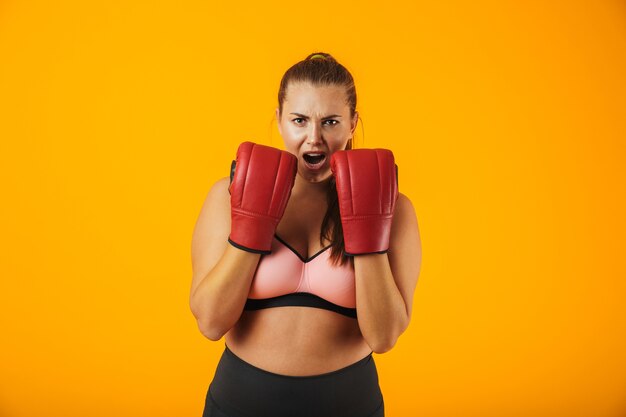 Portrait de la belle grande femme en soutien-gorge sportive portant des gants de boxe pratiquant, isolé sur fond jaune