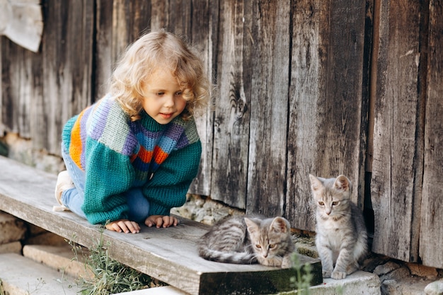 Portrait d'une belle et heureuse fille bouclée dans un pull tricoté jouant avec un chaton près d'un mur en bois