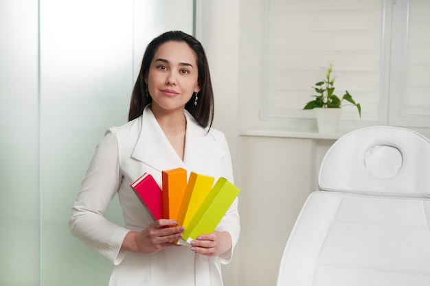 Portrait d'une belle infirmière brune souriante ou d'un médecin portant une boîte de tenue de cosmétologue en blouse blanche