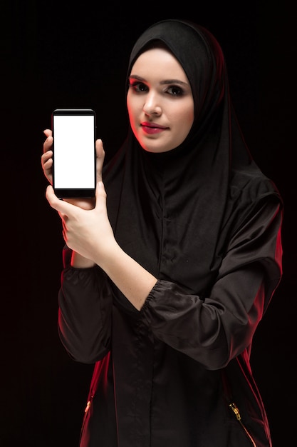 Portrait de belle intelligente jeune femme musulmane portant le hijab noir publicité téléphone mobile dans ses mains comme concept d'éducation noir