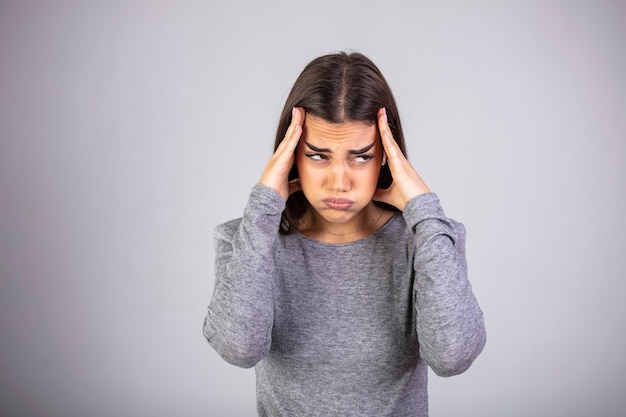 Portrait de la belle jeune brune touchant ses tempes ressentant du stress, sur fond gris.