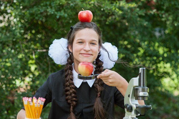 Portrait d'une belle jeune écolière regardant à travers une loupe et assise à un bureau