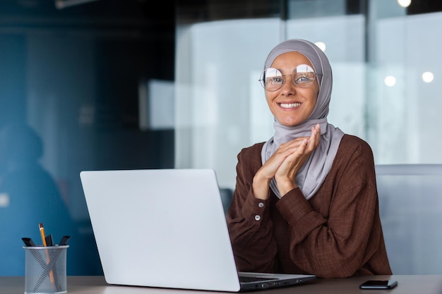 Portrait d'une belle jeune étudiante arabe dans un hijab assis à la table dans le bureau avec