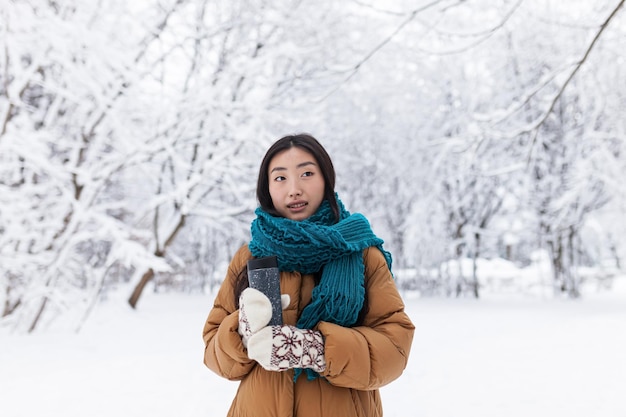 Portrait d'une belle jeune étudiante asiatique adolescente dans un parc à neige d'hiver dans des vêtements chauds une femme en promenade tenant une tasse de boisson chaude