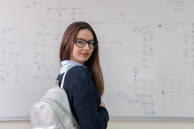 portrait d'une belle jeune étudiante debout devant un tableau blanc et regardant la caméra