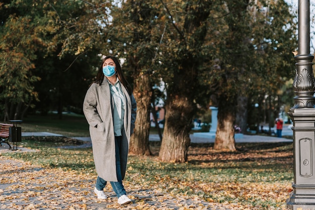 Portrait d'une belle jeune femme adulte sur le fond de l'automne dans le parc dans un masque médical