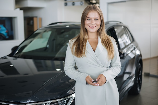 Portrait de belle et jeune femme d'affaires dans la salle d'exposition de voitures femme tenant les clés de sa nouvelle voiture