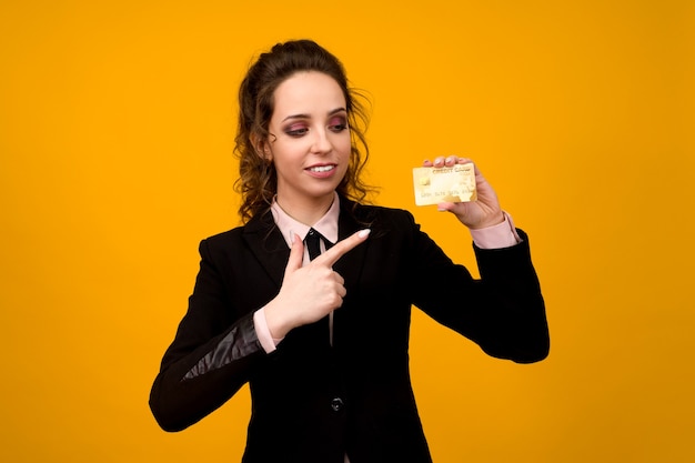Portrait d'une belle jeune femme d'affaires debout isolé sur fond jaune, tenant une carte de crédit