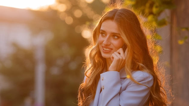 Portrait d'une belle jeune femme d'affaires réussie caucasienne fille du millénaire modèle féminin se tient à l'extérieur dans la ville lever du soleil fond de soleil coucher de soleil parler sur téléphone mobile répond appel appelant parler