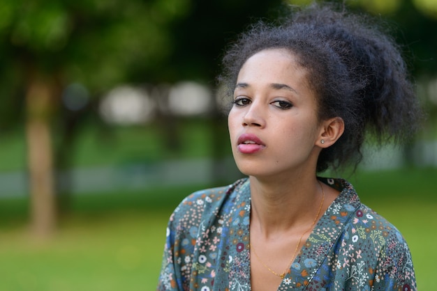 Portrait de la belle jeune femme africaine aux cheveux afro se détendre dans le parc en plein air