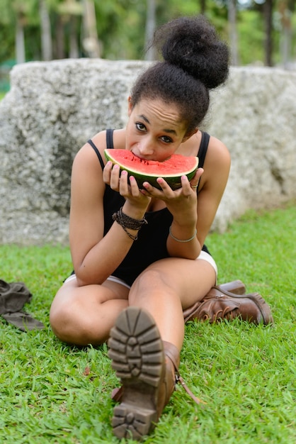 Portrait de la belle jeune femme africaine aux cheveux afro se détendre dans le parc en plein air