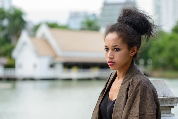 Portrait de la belle jeune femme africaine aux cheveux afro se détendre dans le parc en plein air