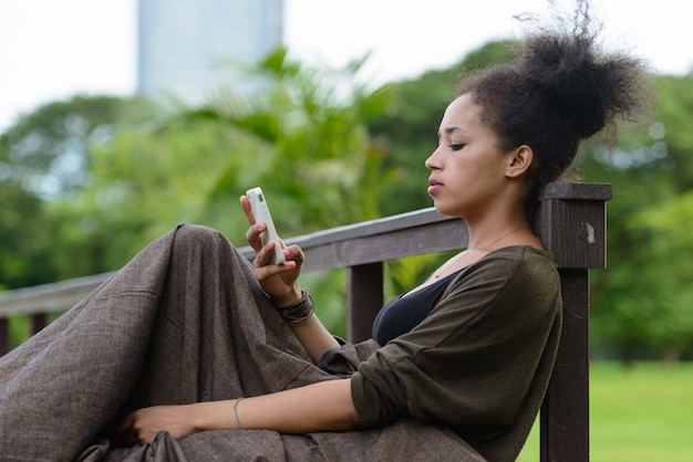 Portrait de la belle jeune femme africaine aux cheveux afro se détendre dans le parc en plein air