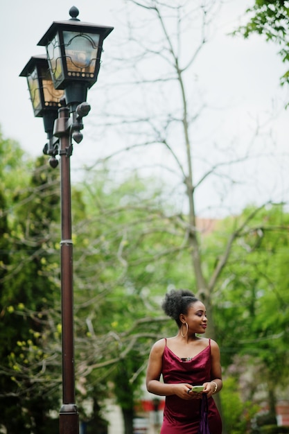 Portrait d'une belle jeune femme africaine naturelle aux cheveux afro. Modèle noir en robe de soie rouge avec téléphone portable.