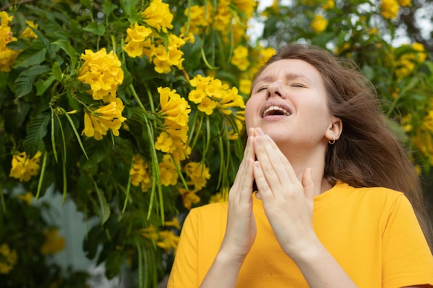 Portrait d'une belle jeune femme allergique souffrant d'allergie au pollen ou de froid sur fond d'arbre en fleurs de fleurs naturelles au printemps ou en été ensoleillé éternue soufflant son nez qui coule se frotte les yeux