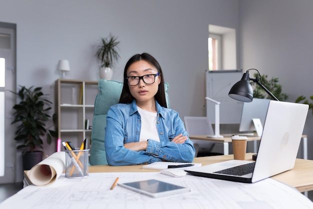 Portrait d'une belle jeune femme asiatique architecte dans des verres travaillant à un bureau devant un ordinateur et