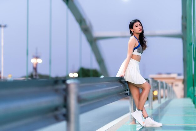 Portrait d'une belle jeune femme asiatique athlétique en vêtements de sport à la mode debout et se reposant après un entraînement physique sur la route en faisant du jogging ou en faisant du vélo et en faisant de l'exercice sur le pont