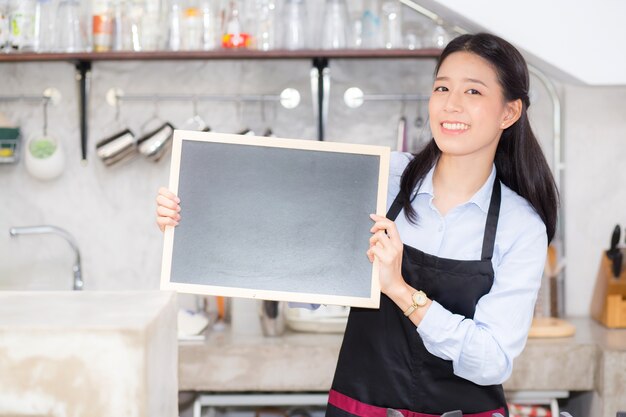 Portrait belle jeune femme asiatique barista est un employé debout tenant tableau.