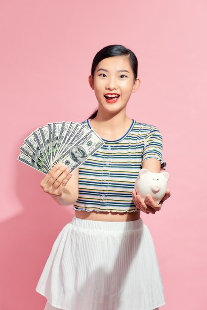 Portrait belle jeune femme asiatique avec beaucoup d'argent et d'argent avec tirelire sur fond isolé rose