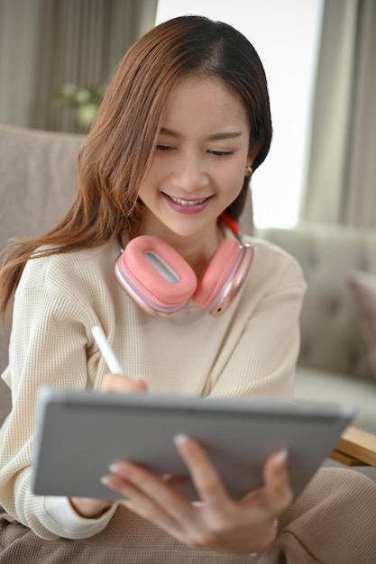 Portrait Belle jeune femme asiatique avec un casque à l'aide d'une tablette numérique dans son salon