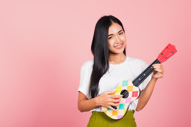 Portrait d'une belle jeune femme asiatique heureuse, adolescente, confiante, visage souriant, tenir la guitare acoustique Ukulele, femme jouant de la petite guitare hawaïenne, prise de vue en studio isolée sur fond rose, avec espace de copie