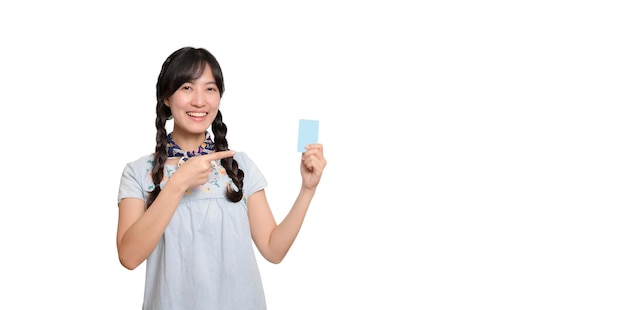 Portrait d'une belle jeune femme asiatique heureuse en robe denim tenant une carte de crédit sur fond blanc